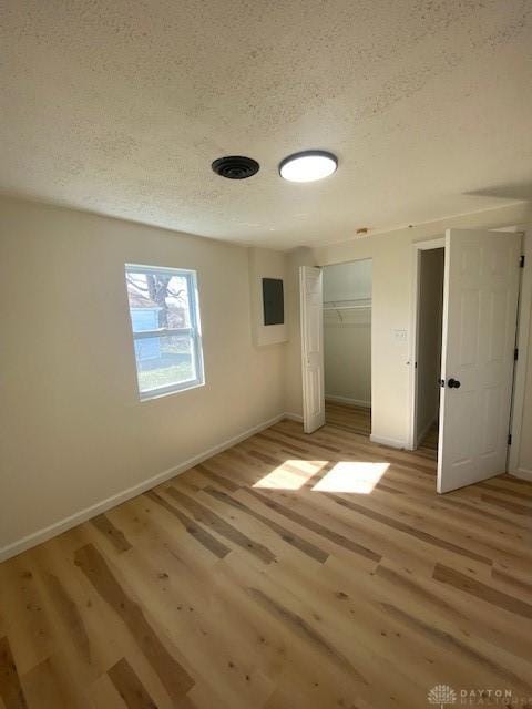 unfurnished room featuring light wood-style flooring, a textured ceiling, and baseboards