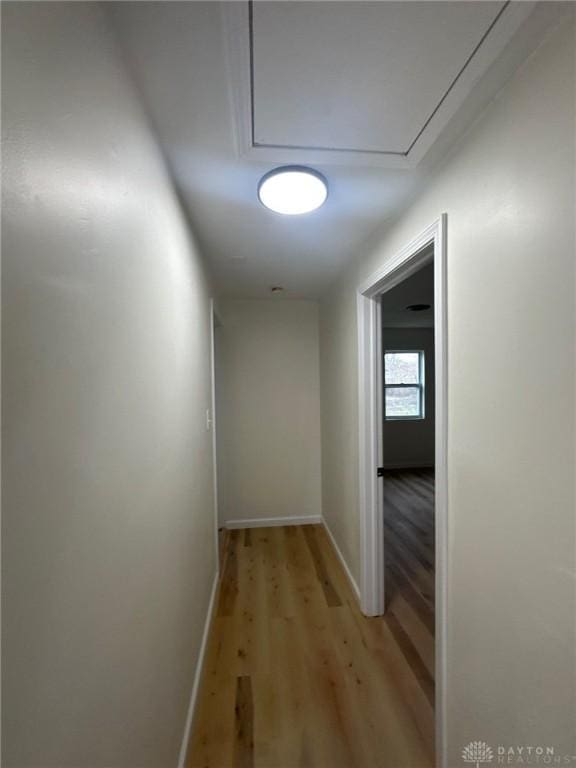 hallway featuring attic access, light wood-style flooring, and baseboards