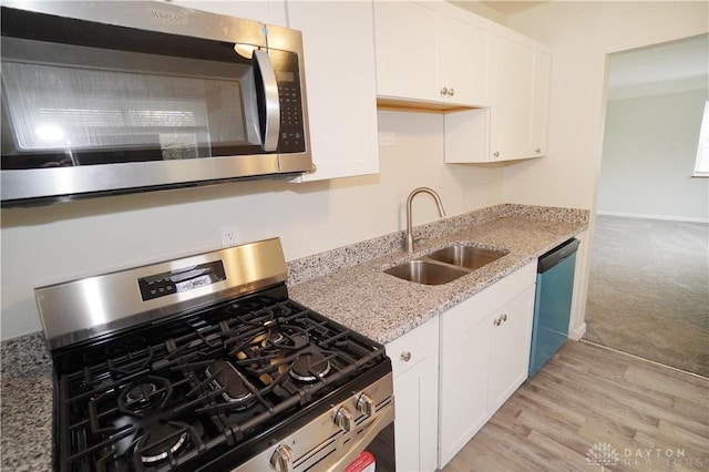 kitchen with light stone countertops, light wood-type flooring, stainless steel appliances, white cabinetry, and a sink