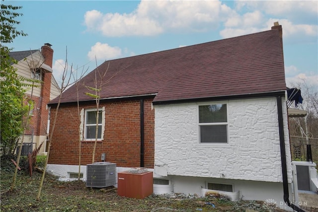 view of side of property featuring brick siding, central air condition unit, roof with shingles, and stone siding