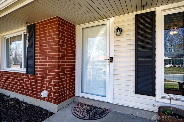 doorway to property featuring a porch and brick siding