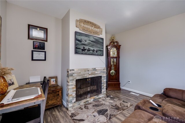 living area with visible vents, baseboards, a stone fireplace, and wood finished floors