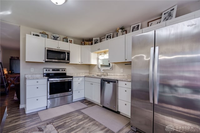 kitchen featuring light stone counters, stainless steel appliances, wood finished floors, white cabinetry, and a sink