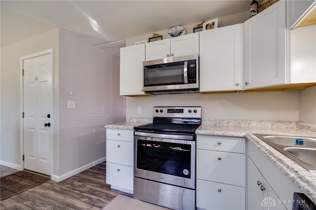 kitchen featuring baseboards, dark wood-style flooring, a sink, stainless steel appliances, and white cabinetry