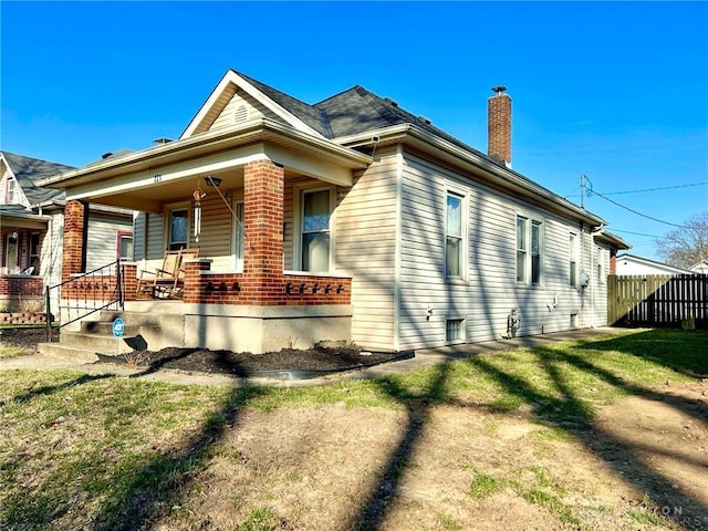 view of side of home with a lawn, a porch, a chimney, and fence