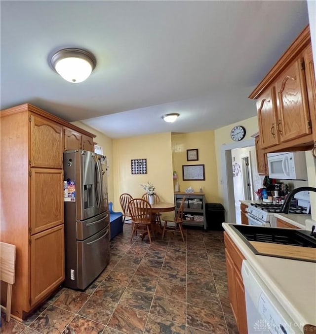 kitchen with white appliances, a sink, light countertops, stone finish flooring, and brown cabinets