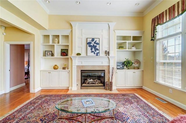 living room featuring crown molding, light wood-style flooring, a fireplace with flush hearth, and a healthy amount of sunlight