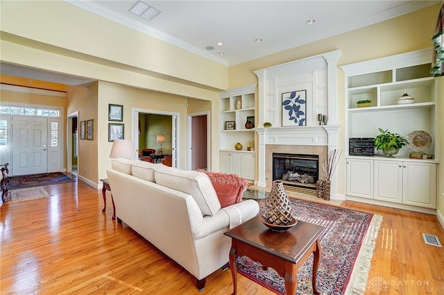 living area featuring built in shelves, visible vents, light wood finished floors, a high end fireplace, and ornamental molding