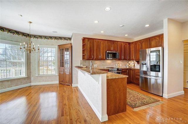 kitchen with light stone counters, tasteful backsplash, stainless steel appliances, light wood-style floors, and a peninsula