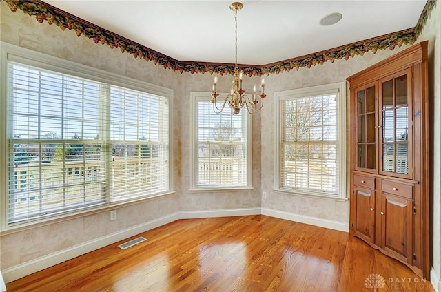 unfurnished dining area with visible vents, baseboards, an inviting chandelier, and light wood-style flooring