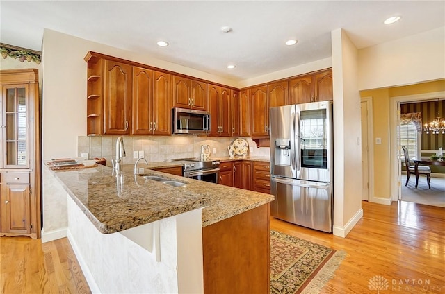 kitchen with light wood finished floors, light stone counters, a peninsula, stainless steel appliances, and open shelves