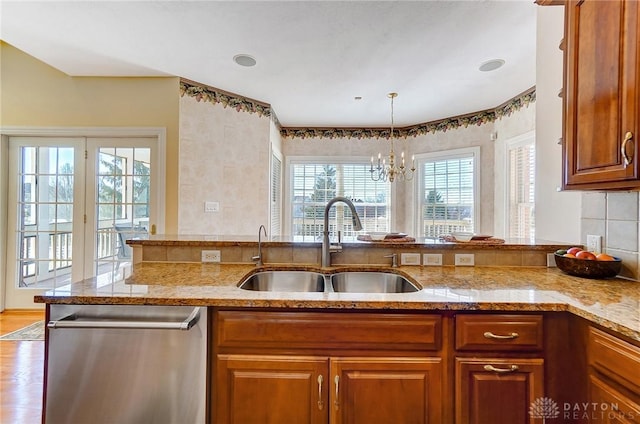 kitchen featuring stainless steel dishwasher, light stone counters, brown cabinetry, and a sink