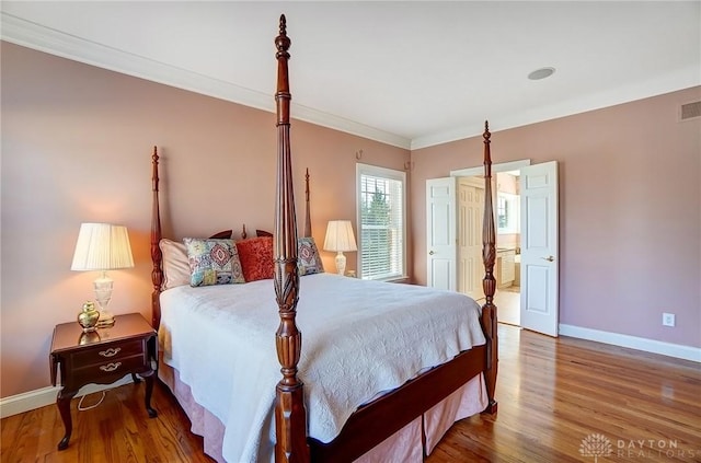 bedroom featuring visible vents, baseboards, wood finished floors, and crown molding