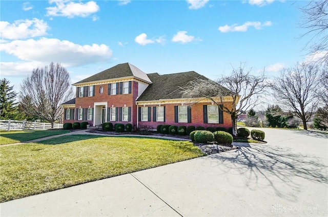 colonial-style house featuring driveway, brick siding, a front lawn, and fence