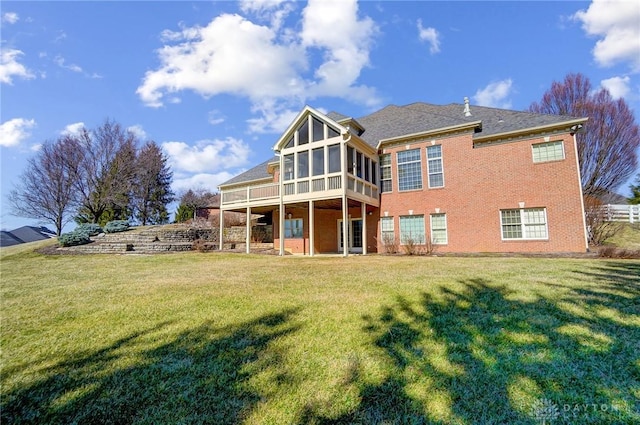 back of property featuring a yard, brick siding, and a sunroom