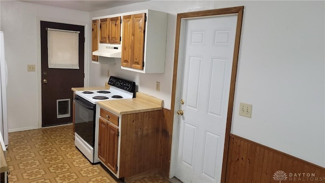 kitchen featuring a wainscoted wall, under cabinet range hood, electric range oven, light countertops, and light floors