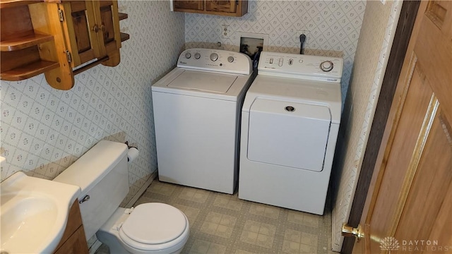 laundry room featuring a sink, separate washer and dryer, wallpapered walls, light floors, and laundry area