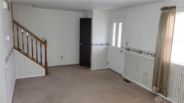 entrance foyer featuring stairway, visible vents, wainscoting, and carpet flooring