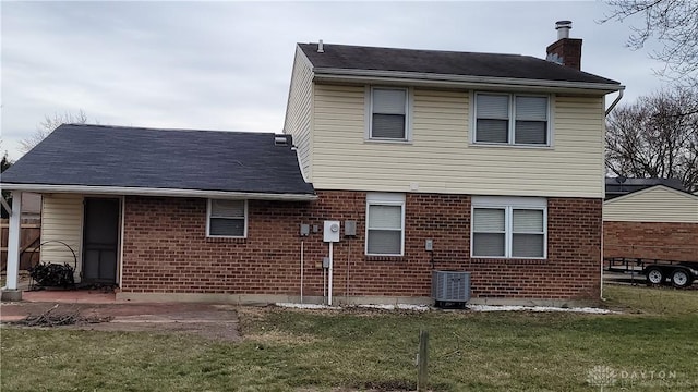 rear view of property with a yard, brick siding, central AC, and a chimney