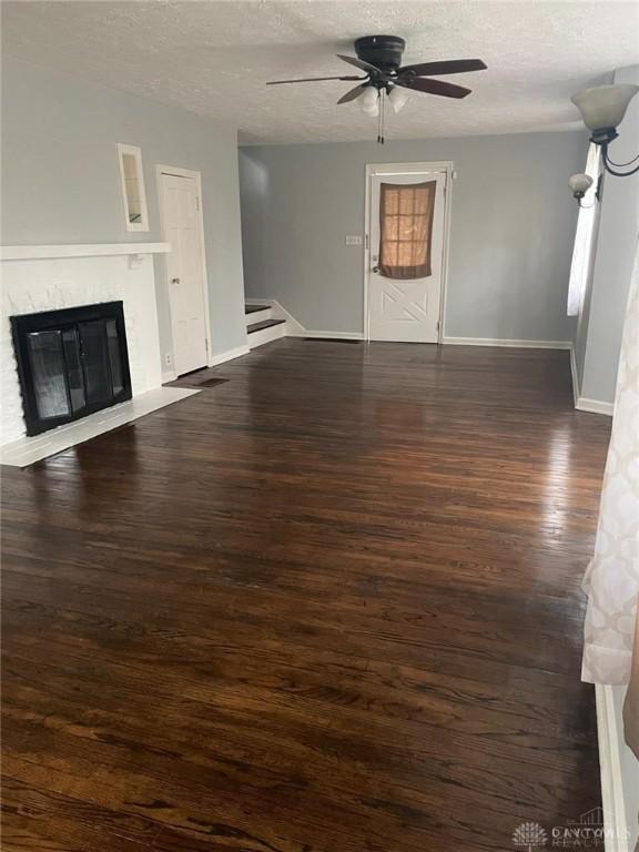 unfurnished living room featuring baseboards, ceiling fan, dark wood finished floors, a glass covered fireplace, and a textured ceiling