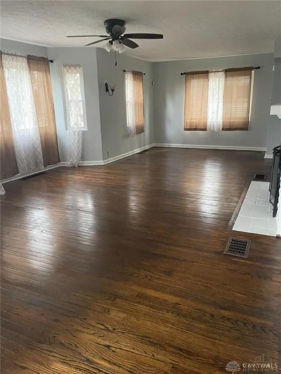 unfurnished living room with visible vents, baseboards, a ceiling fan, and dark wood-style flooring