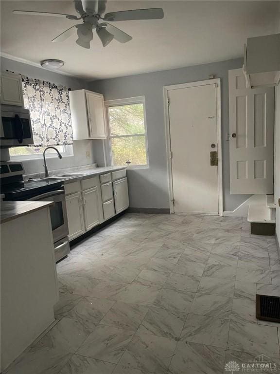 kitchen featuring baseboards, a sink, stainless steel appliances, white cabinets, and marble finish floor