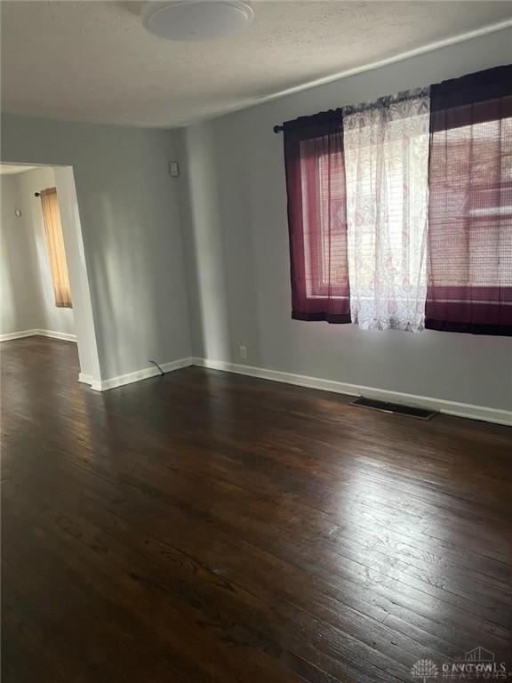 empty room featuring visible vents, wood-type flooring, and baseboards