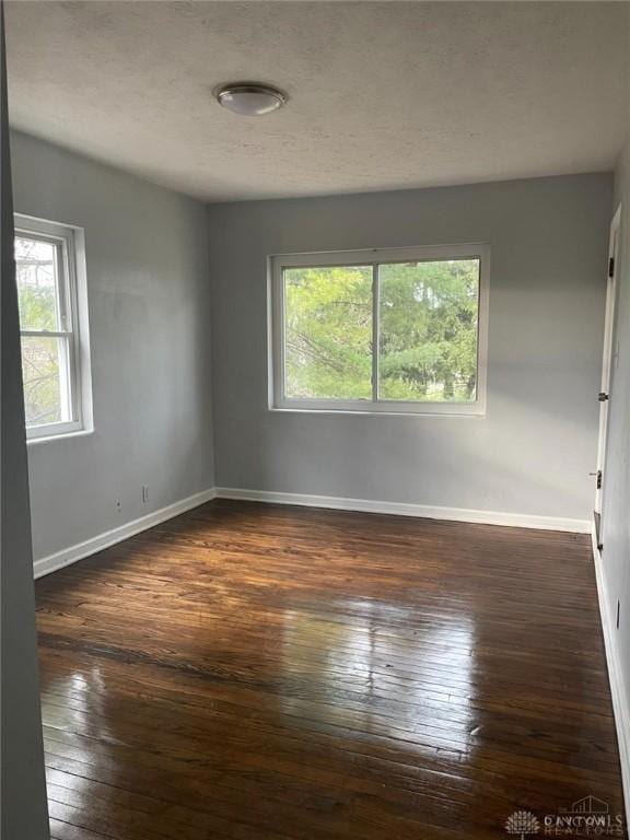 empty room with baseboards, dark wood-style flooring, a wealth of natural light, and a textured ceiling