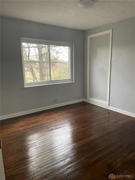 empty room featuring a textured ceiling, baseboards, and dark wood-style flooring