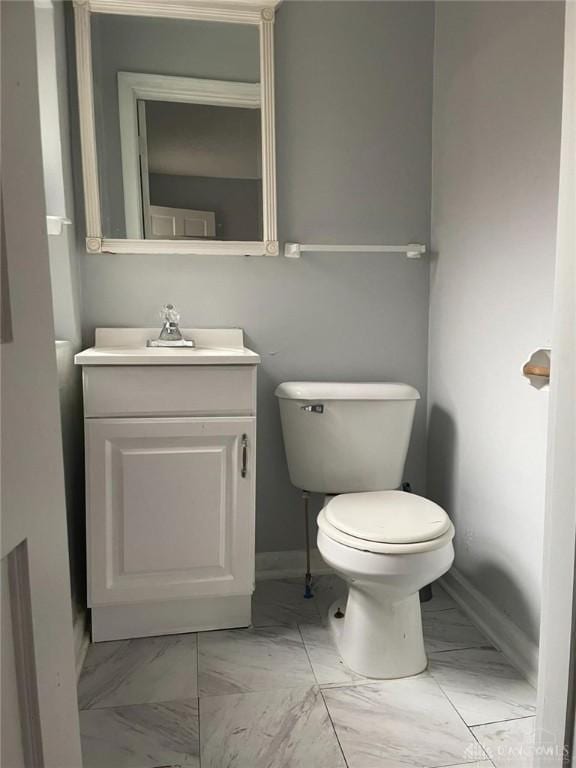 half bath with vanity, toilet, baseboards, and marble finish floor