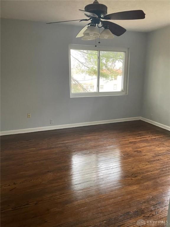 empty room featuring baseboards, dark wood-style flooring, and ceiling fan