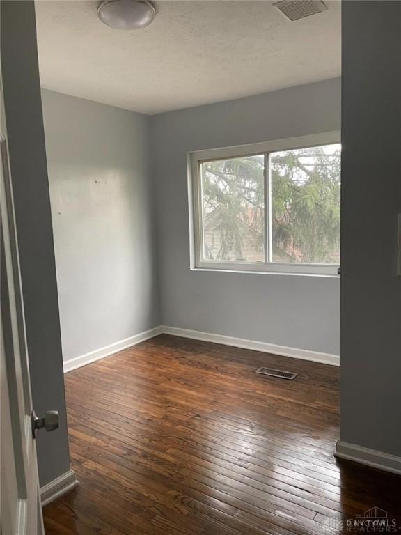 empty room featuring visible vents, baseboards, and dark wood-style flooring