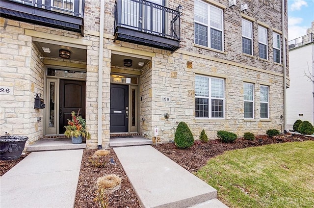 view of exterior entry featuring stone siding and a balcony