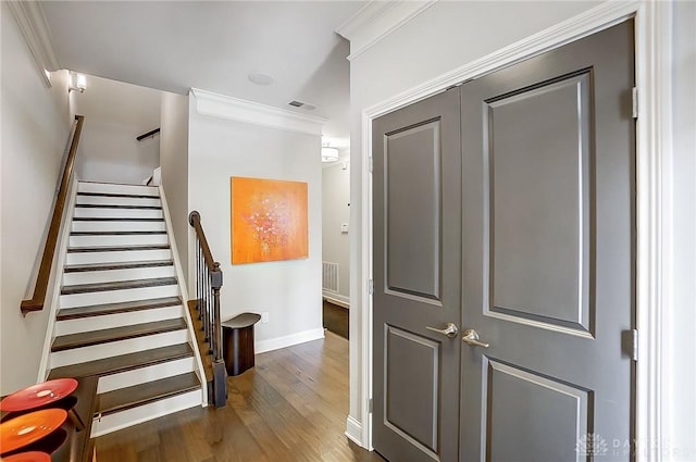 staircase featuring visible vents, crown molding, baseboards, and wood finished floors