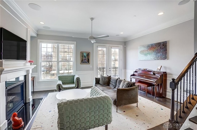 living room featuring wood finished floors, a glass covered fireplace, wainscoting, crown molding, and stairs