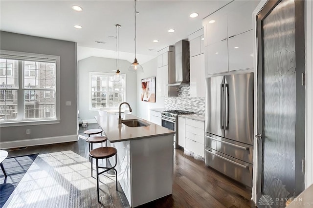 kitchen featuring modern cabinets, a sink, stainless steel appliances, wall chimney range hood, and decorative backsplash