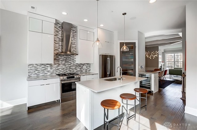 kitchen featuring a kitchen bar, modern cabinets, appliances with stainless steel finishes, wall chimney exhaust hood, and decorative backsplash