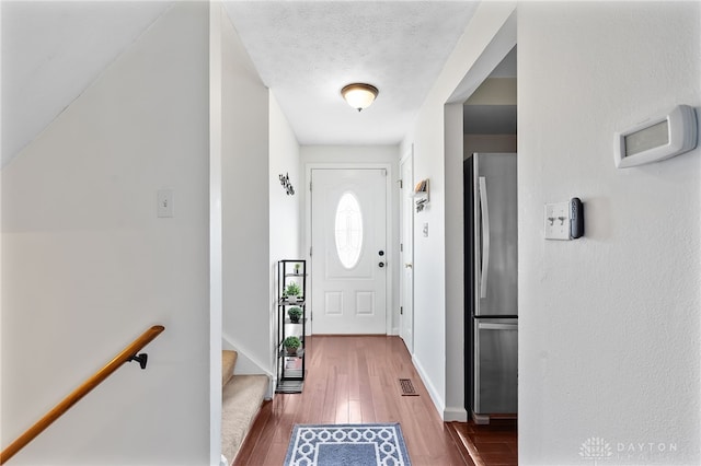 doorway featuring visible vents, hardwood / wood-style flooring, a textured ceiling, stairway, and baseboards