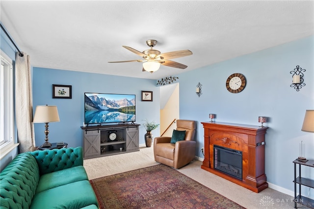 carpeted living room with ceiling fan, baseboards, and a glass covered fireplace