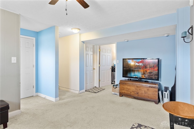 carpeted living area with baseboards and ceiling fan