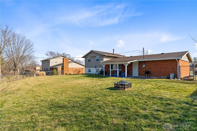 rear view of property featuring a yard, brick siding, an outdoor fire pit, and fence