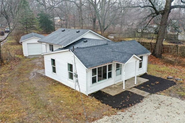 rear view of property featuring an outdoor structure, fence, and a shingled roof