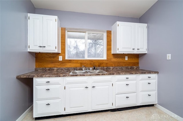 kitchen featuring dark countertops, white cabinets, baseboards, and a sink