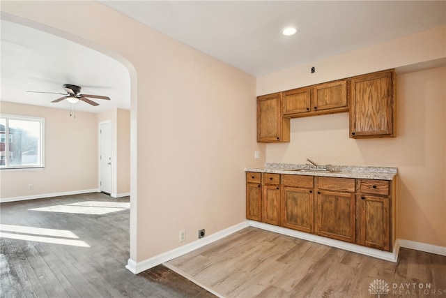 kitchen featuring a sink, brown cabinetry, arched walkways, and light wood-type flooring