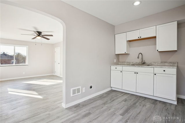 kitchen featuring visible vents, light countertops, arched walkways, white cabinetry, and a sink