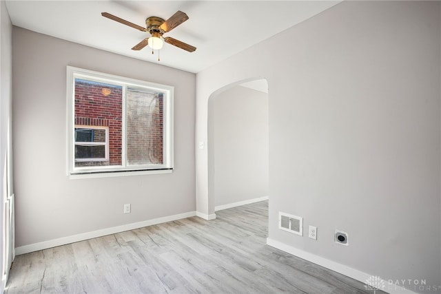 empty room featuring a ceiling fan, wood finished floors, visible vents, baseboards, and arched walkways