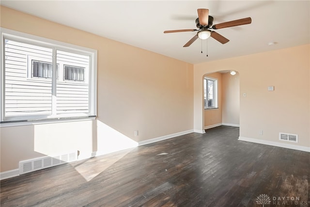 unfurnished room with arched walkways, visible vents, dark wood finished floors, and baseboards