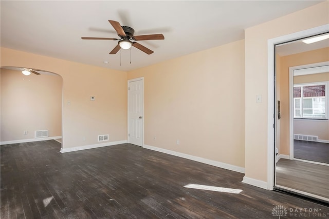 empty room featuring dark wood-type flooring, visible vents, arched walkways, and baseboards