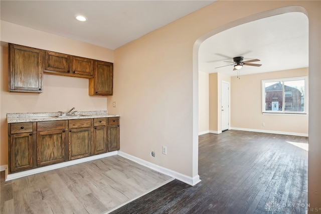 kitchen with baseboards, light countertops, wood finished floors, arched walkways, and a sink