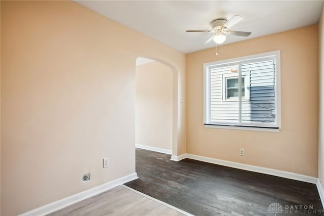 unfurnished room with arched walkways, a ceiling fan, baseboards, and wood finished floors